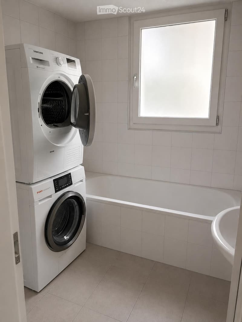 Bathroom with a bathtub, sink, and stacked washing machine and dryer unit.