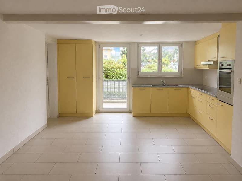 Bright kitchen with light yellow cabinets, white tiled floor, and a window overlooking a green area.