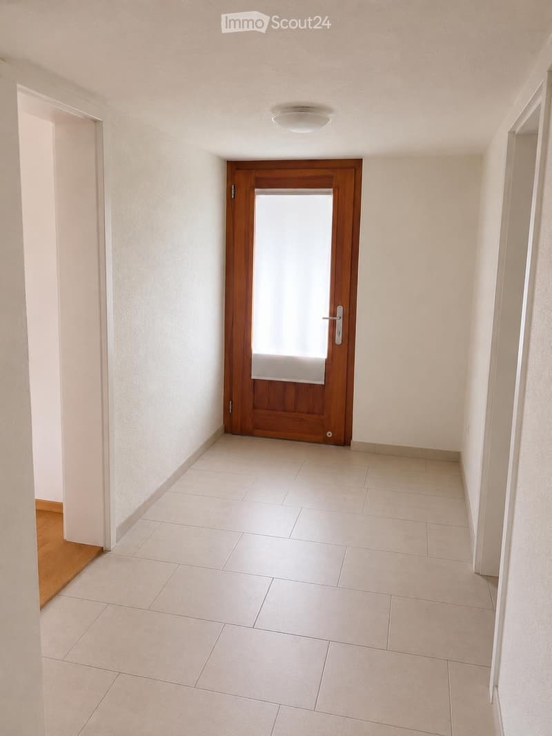 Empty hallway with tiled floor, white walls, and a wooden door at the end.
