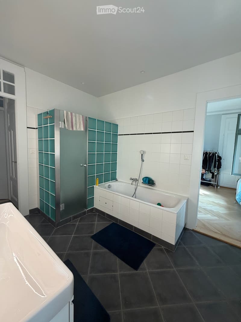 Modern bathroom with white tiled walls, dark tiled floor, bathtub, shower stall with glass doors, and a bathmat on the floor.