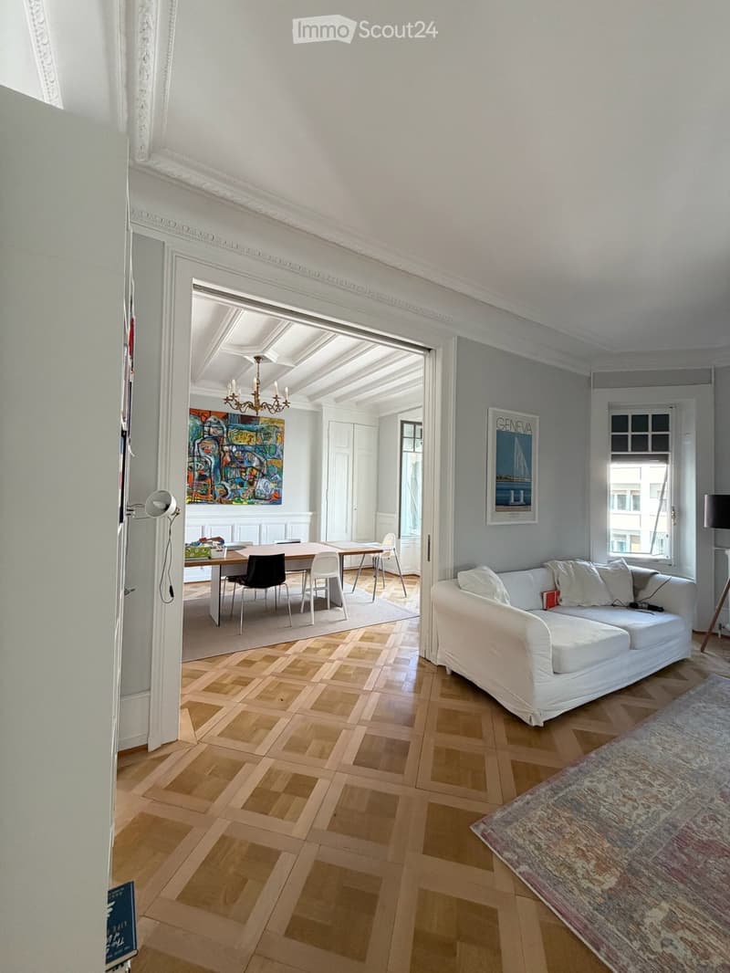 Open-concept living and dining area with a white sofa, dining table, chairs, and artwork on the walls.
