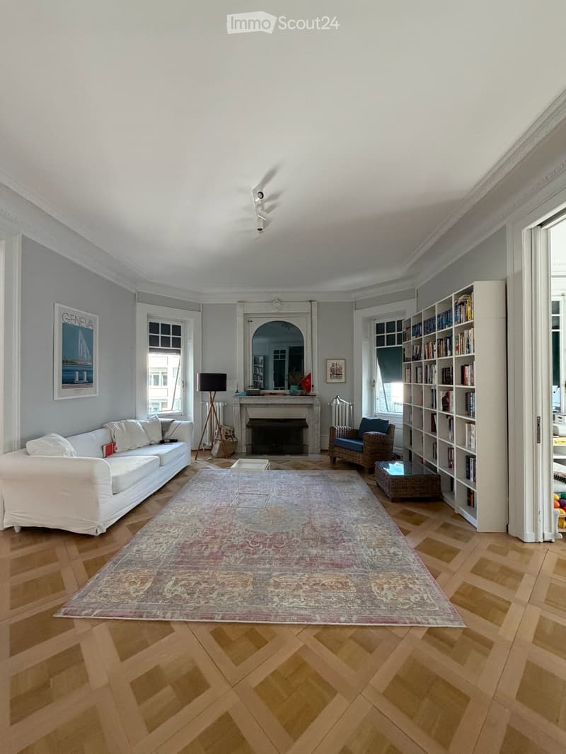 Living room with white sofa, armchair, bookshelf, coffee table, floor lamp, fireplace, and a large area rug on a wooden floor.