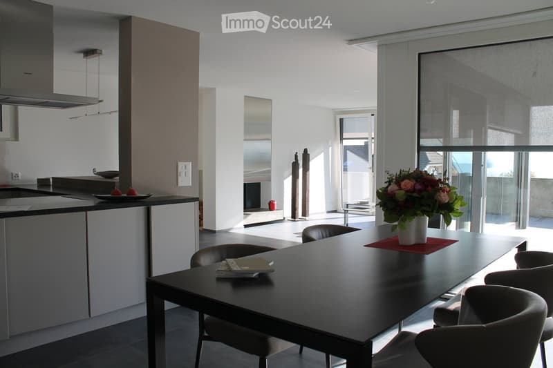 Modern open-plan kitchen and dining area with a black dining table, chairs, a flower vase, and a kitchen island with a sink and faucet.