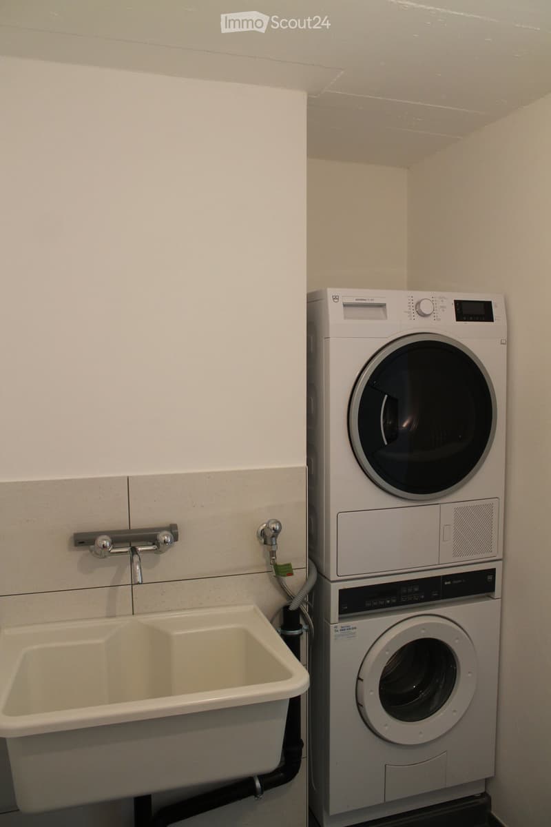 Bathroom with a washing machine and dryer stacked vertically, a sink with a faucet, and a tiled wall.