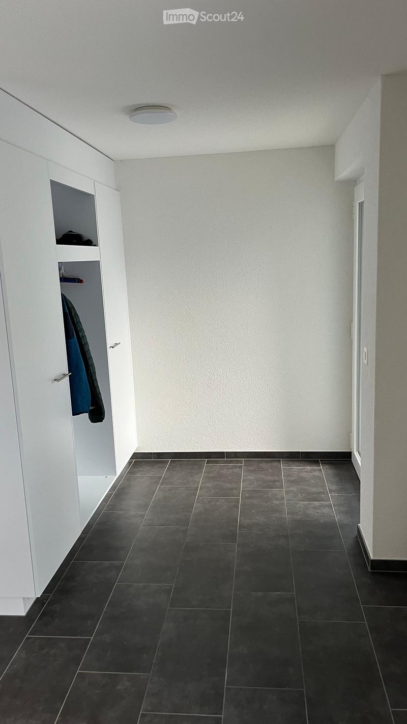 Empty hallway with dark grey tiled floor, white walls, and a built-in white closet with clothes inside.