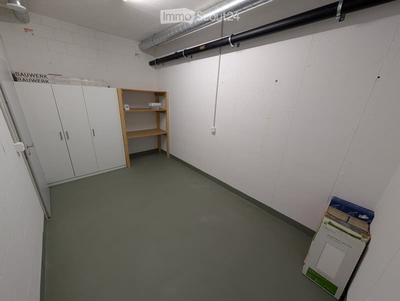 A small, unfurnished storage room with white walls, a grey floor, a white cabinet, and a wooden shelf holding a few items.