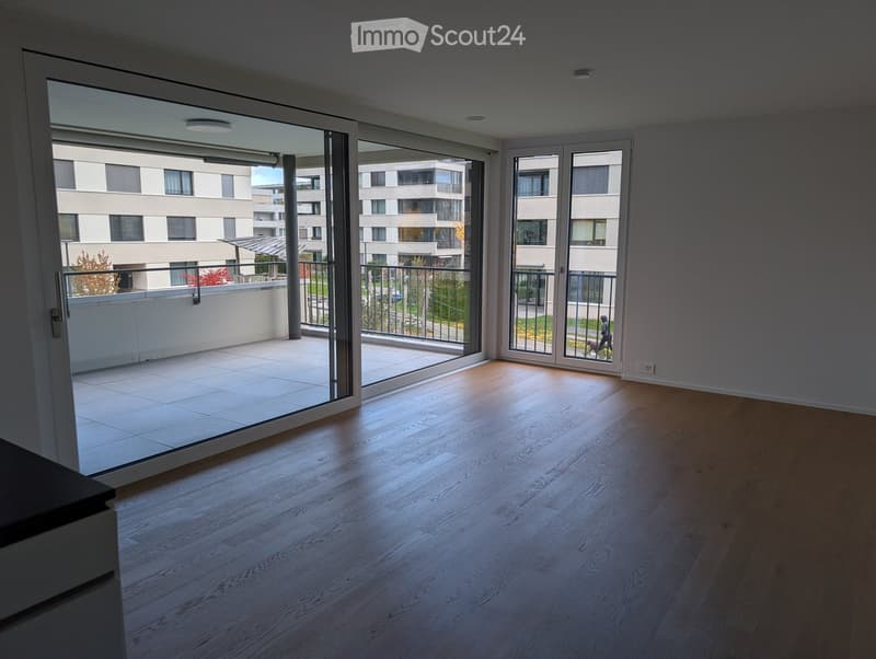 Empty room with wooden flooring and large glass sliding doors leading to a balcony. The balcony has a tiled floor and metal railing.