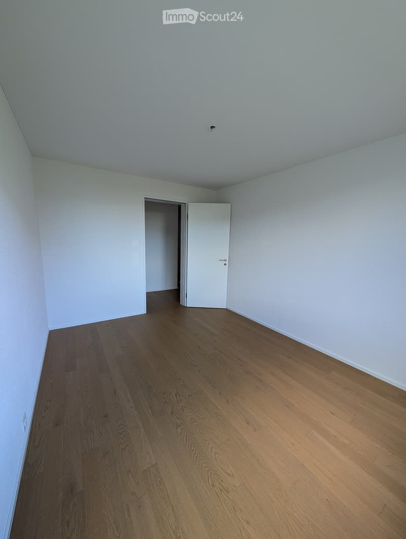 Empty room with light blue walls and wooden flooring, featuring a white door and visible electrical outlets.