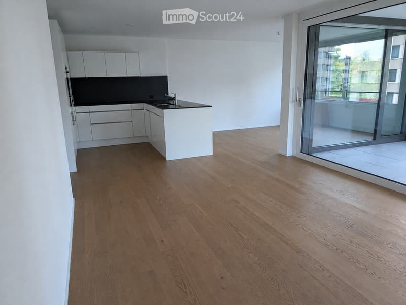 Modern, unfurnished kitchen with white cabinets, a black countertop, and a wooden floor. Features a large sliding glass door leading to a balcony.