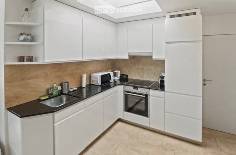 Modern kitchen with white cabinets, black countertop, stainless steel sink, microwave, oven, and refrigerator. Features a built-in hood and open shelving with decorative items.