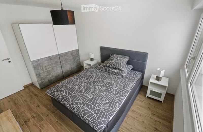 Modern bedroom with a grey headboard bed, patterned bedding, white nightstands, and a large wardrobe with a grey and white design.