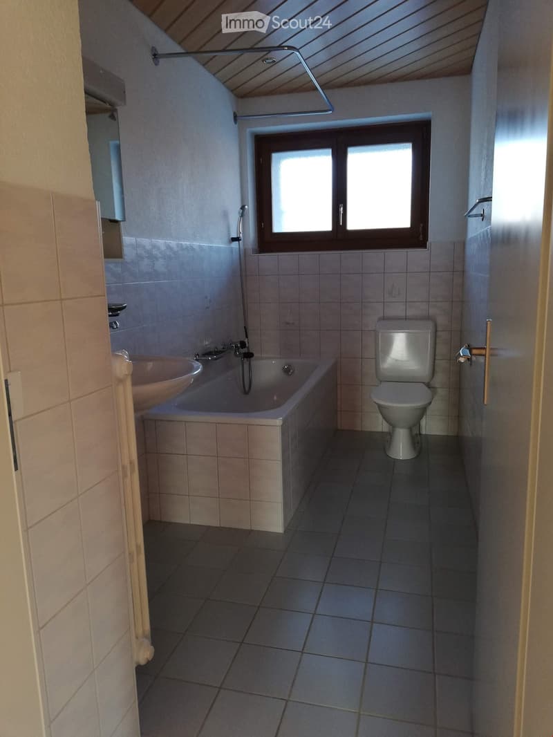 Bathroom with a bathtub, toilet, sink, and a window with frosted glass panes. The room features tiled walls and floor, and a showerhead is mounted on the wall.