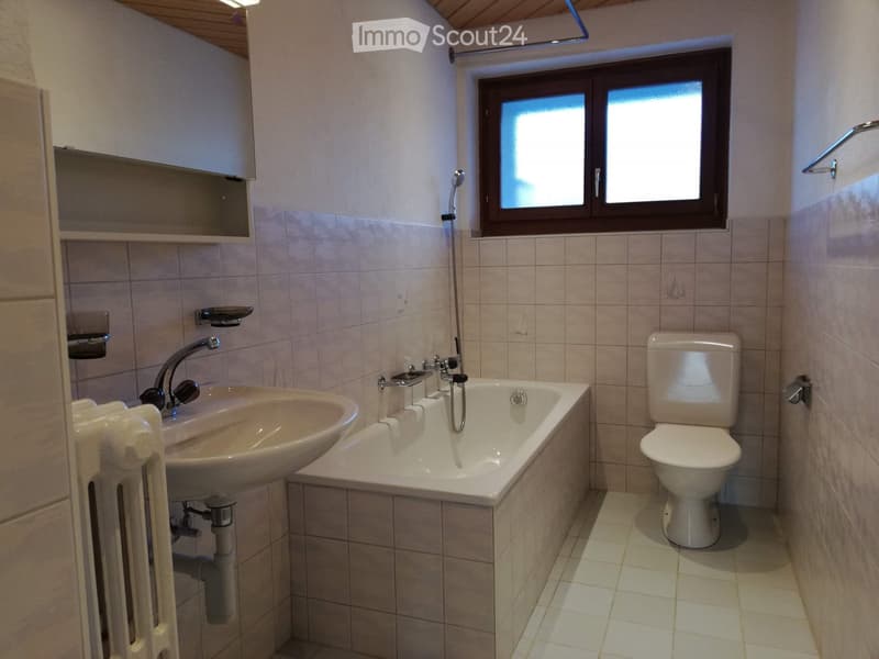 Bathroom with a sink, bathtub, toilet, and a window above the bathtub. The walls are tiled, and there is a radiator on the left side.