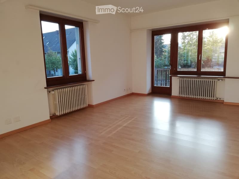 Empty room with wooden flooring, large windows, radiators, and white walls.