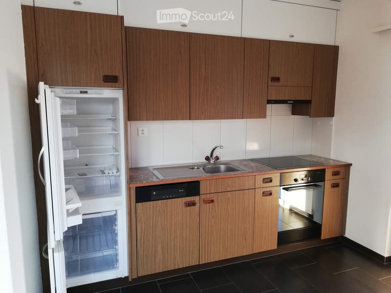 Modern kitchen with wooden cabinets, stainless steel appliances, and a black tiled floor.