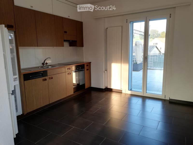 Modern kitchen with wooden cabinets, dark tiled floor, and large sliding glass doors leading to a balcony.