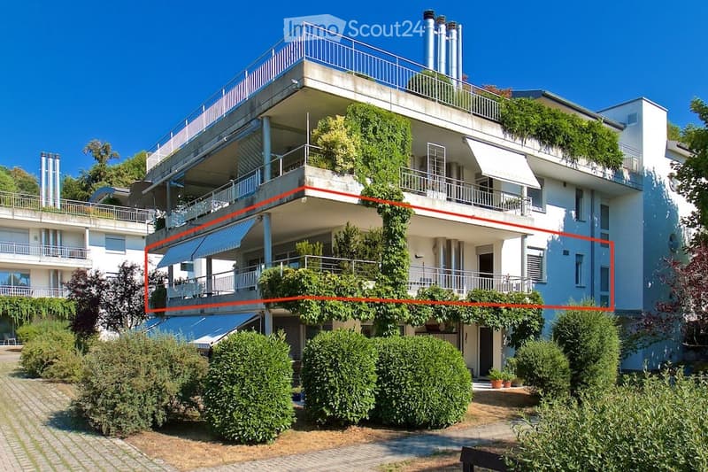 Multi-story residential building with balconies, greenery, and a well-maintained garden area.