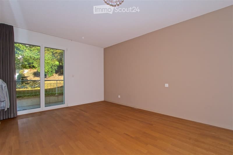 Empty room with wooden flooring, large sliding glass doors leading to a balcony, and neutral-colored walls.