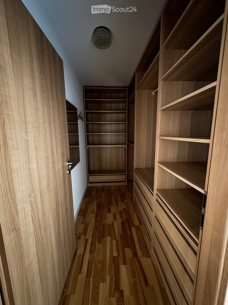 A narrow hallway with wooden flooring and built-in wooden shelving units on both sides, featuring multiple shelves and drawers.