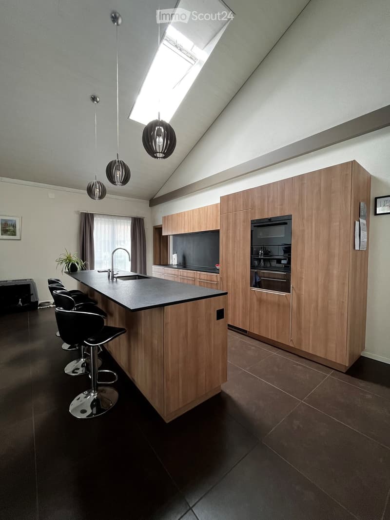 Modern kitchen with wooden cabinets, island, black countertop, and pendant lights. Includes stools, sink, and oven.