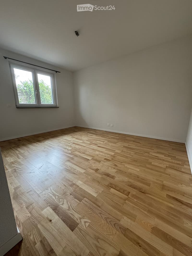 Empty room with wooden flooring, white walls, and a large window with white frame and black curtain rod.