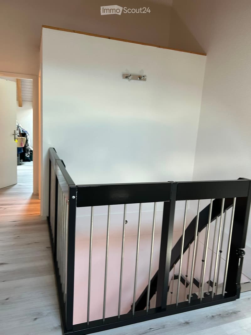 A modern hallway with a wooden floor, white walls, and a black metal baby gate installed on the staircase leading upwards.