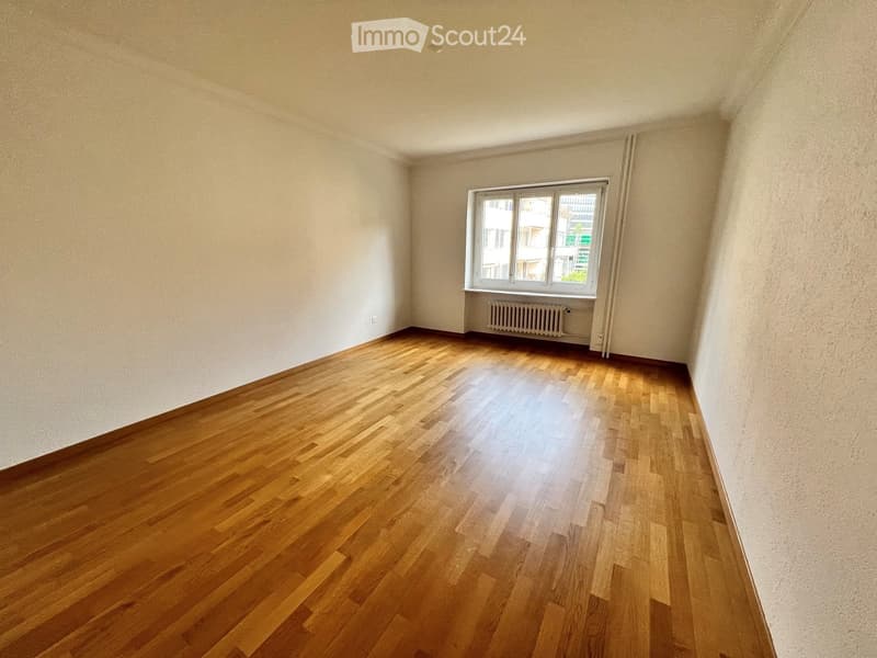 Empty room with wooden flooring, white walls, and a single window with a radiator below it.