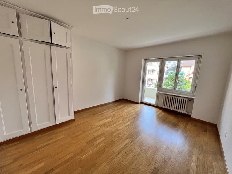 Empty room with wooden flooring, white walls, built-in white closet, and a window with a view of the outside.
