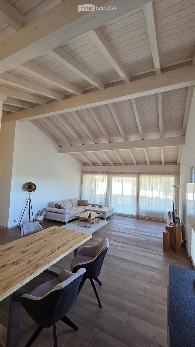 Open-concept living and dining area with exposed wooden beams, white sofa, coffee table, dining table, and chairs.