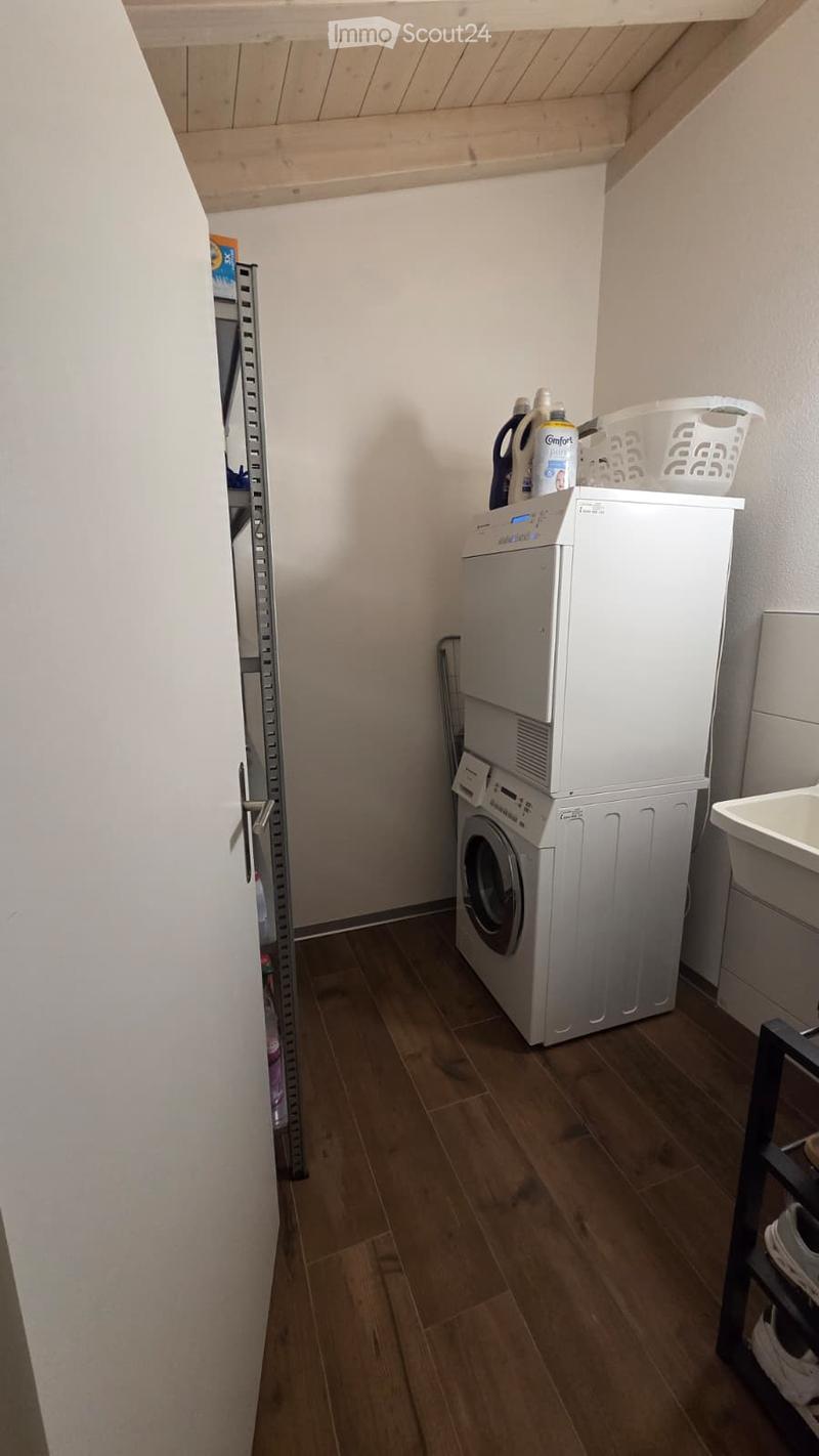 Laundry area with a washing machine, dryer, laundry basket, and shelf. Wooden flooring and white walls.