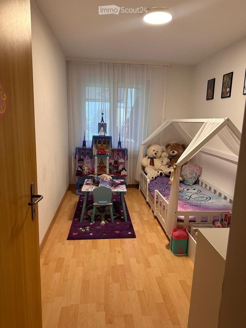 A cozy children's bedroom with a wooden bed, a small table and chair, toys, and a purple rug.