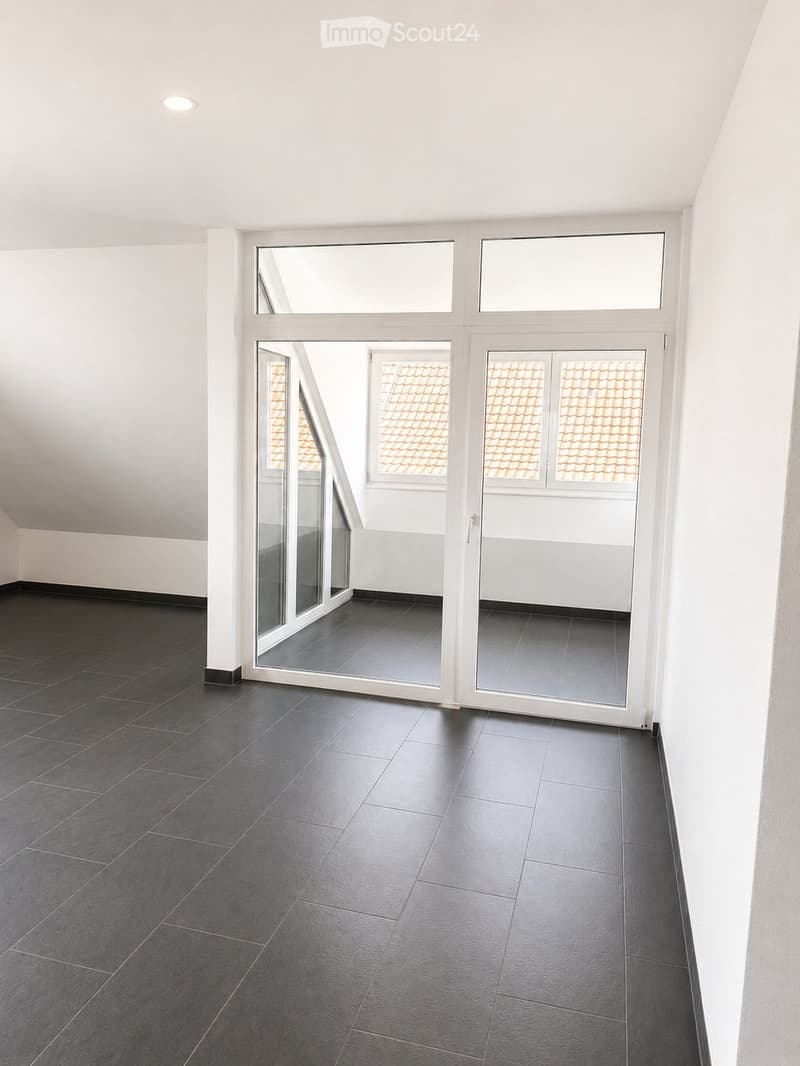 Empty room with dark grey tiled floor, white walls, and large windows with white frames. The room has a modern, minimalist design with a single recessed ceiling light.