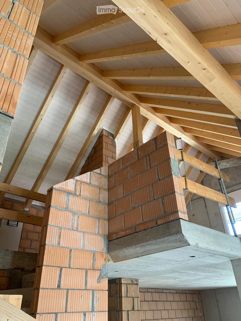 An unfinished attic space with exposed wooden beams and brick walls under construction.