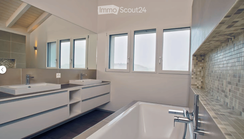 Modern bathroom with a large bathtub, double sink vanity, and large windows providing natural light. The space features sleek, contemporary design elements including a large mirror and modern fixtures.
