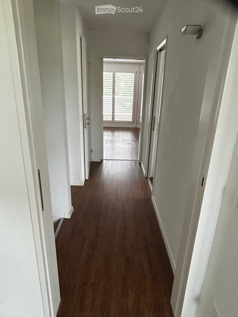 Empty hallway with wooden flooring, white walls, and multiple doors leading to other rooms.