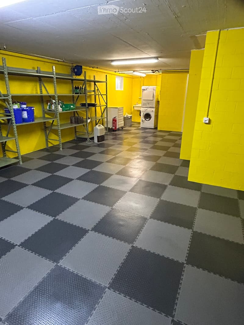 Utility room with yellow walls, checkered floor, washing machine, shelf with cleaning supplies, and a fire extinguisher.