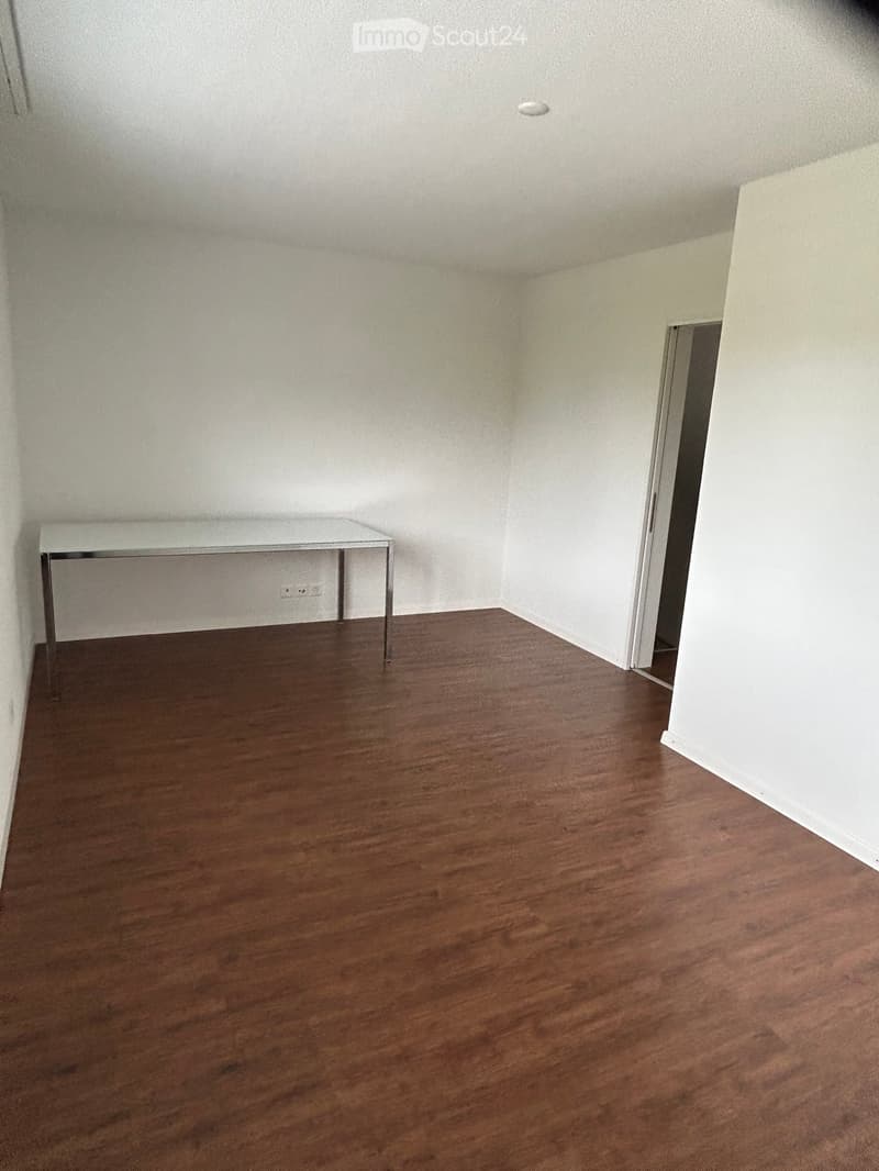 Empty room with wooden flooring and white walls, featuring a small white table against one wall.