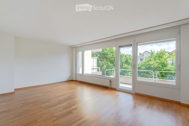 Empty room with wooden flooring, white walls, large windows, and a radiator. No furniture or equipment present.