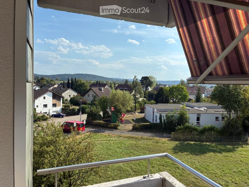 Balcony with a view of a suburban neighborhood, featuring houses, trees, and a clear blue sky.