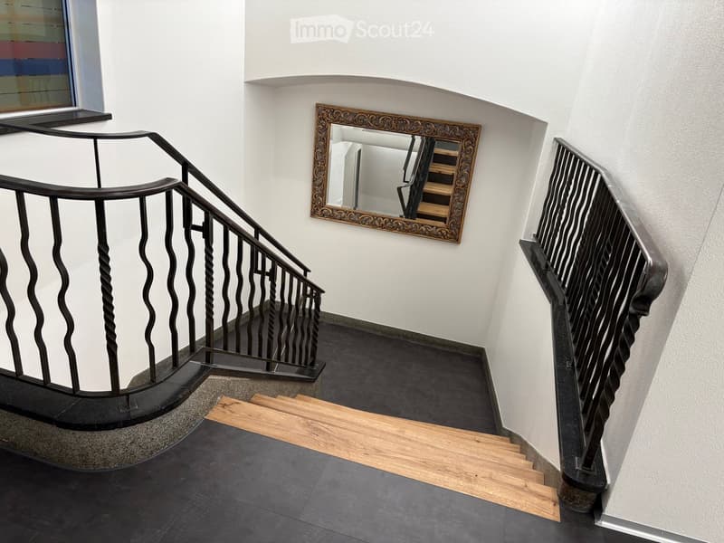 Spiral staircase with wooden steps and black wrought iron railings, white walls, and a decorative mirror on the wall.