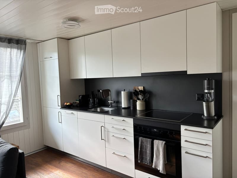 Modern kitchen with white cabinets, black countertops, stainless steel appliances, and a window with curtains.