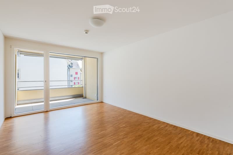 Empty room with wooden flooring, white walls, and large sliding glass doors leading to a balcony.