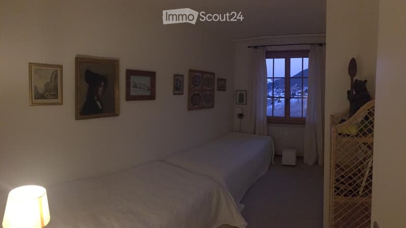Small bedroom, two beds, windows, view of mountains, white walls, wooden furniture, paintings on wall, lamp