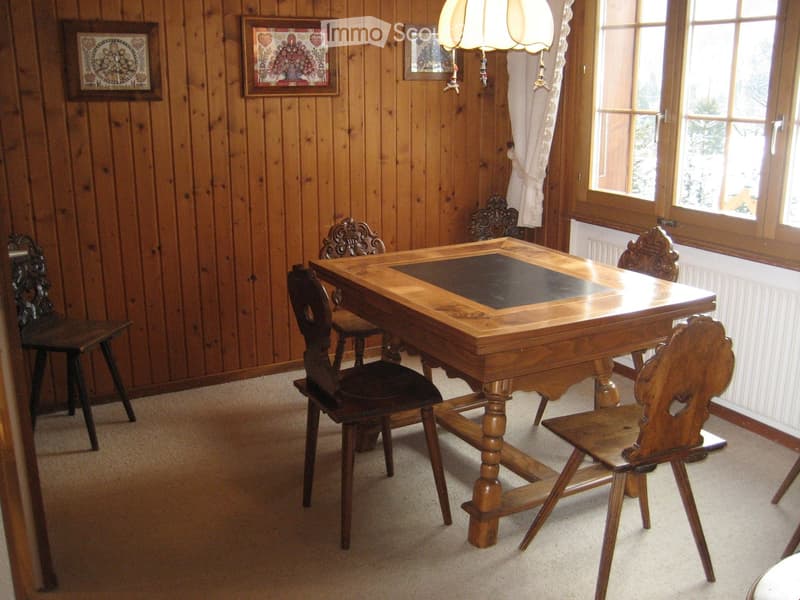 a room with a wooden dining table and chairs, wood paneled walls, framed pictures, and a radiator