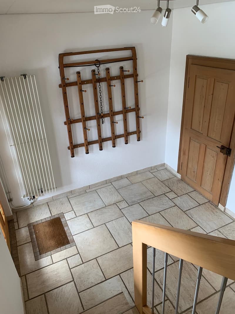 Hallway with tiled floor, wooden door, radiator, and a wooden coat rack with hooks and chains.