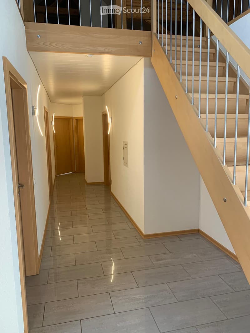 Modern hallway with tiled flooring, wooden staircase with metal railing, and several doors leading to other rooms.