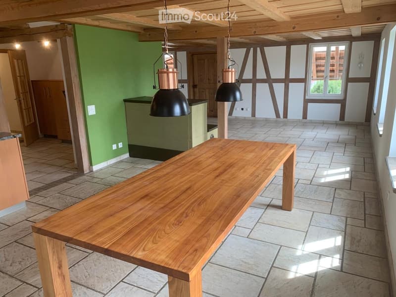 Open-plan space with exposed wooden beams, tiled floor, green walls, and a long wooden table in the center.