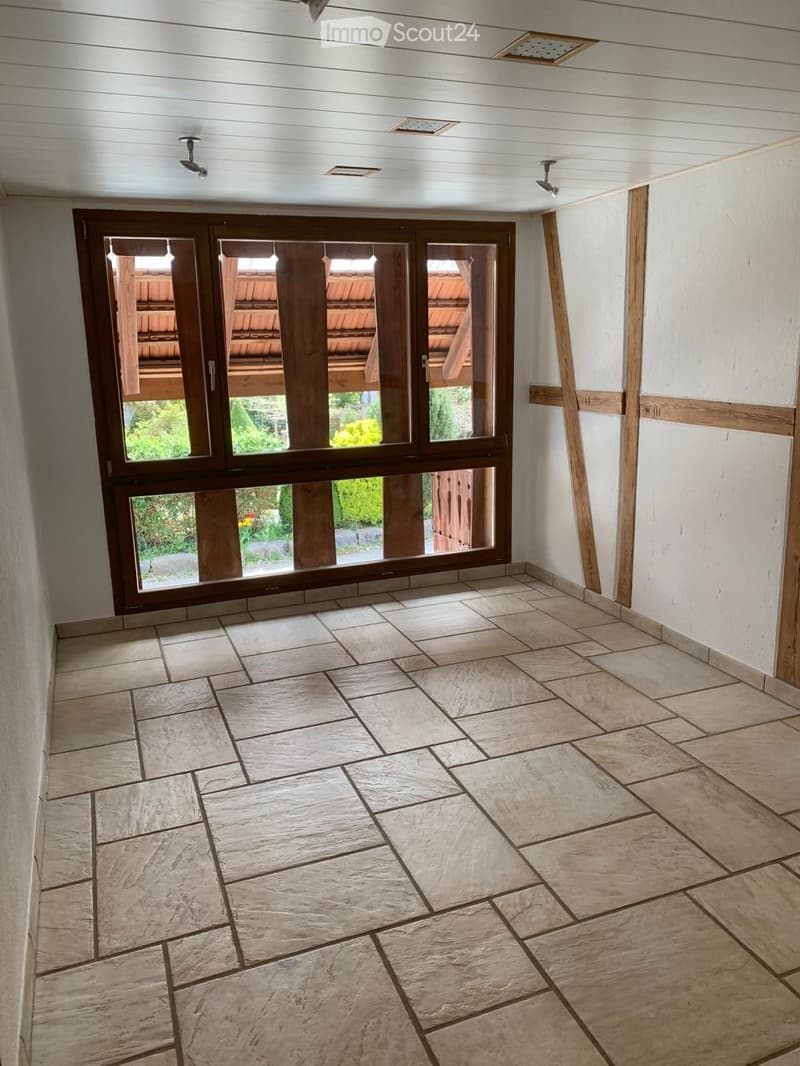 Empty hallway with large wooden-framed glass doors leading to an outdoor area, tiled floor, white walls, and recessed lighting.