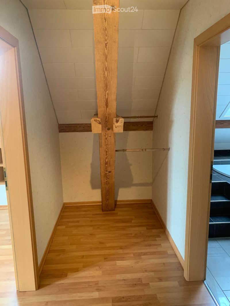 Empty hallway with wooden flooring, white walls, and a wooden structural beam in the center. Natural light filters in from the right side.
