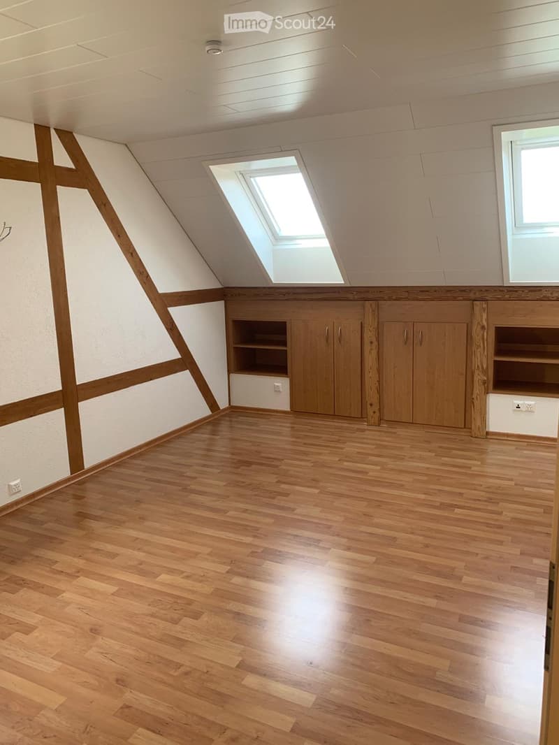 Empty attic room with wooden flooring, white walls, built-in wooden cabinets, and a skylight window.